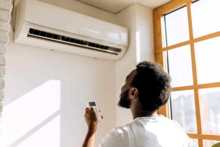 Rear view of young man turning on air conditioner.